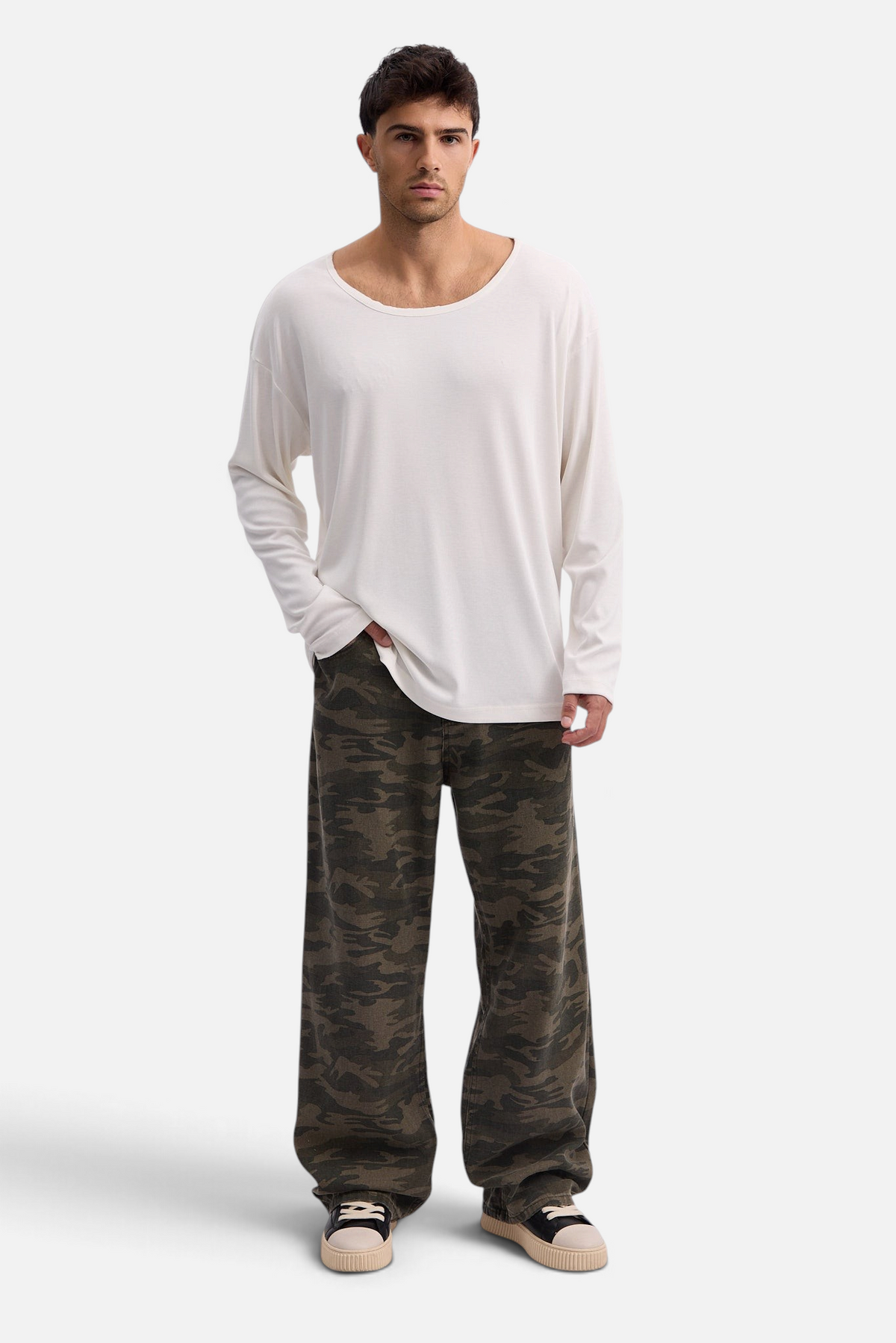 Mainstreamonline baggy army camouflage jeans worn by a model with a white long-sleeve shirt and sneakers