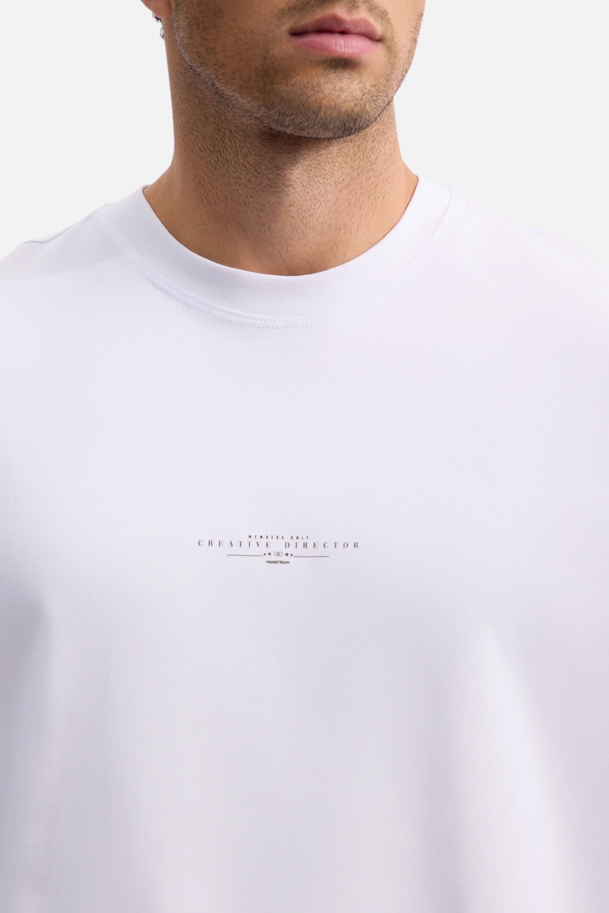 Mainstreamonline white oversized t-shirt with minimalist black Creative Director chest print on a male model