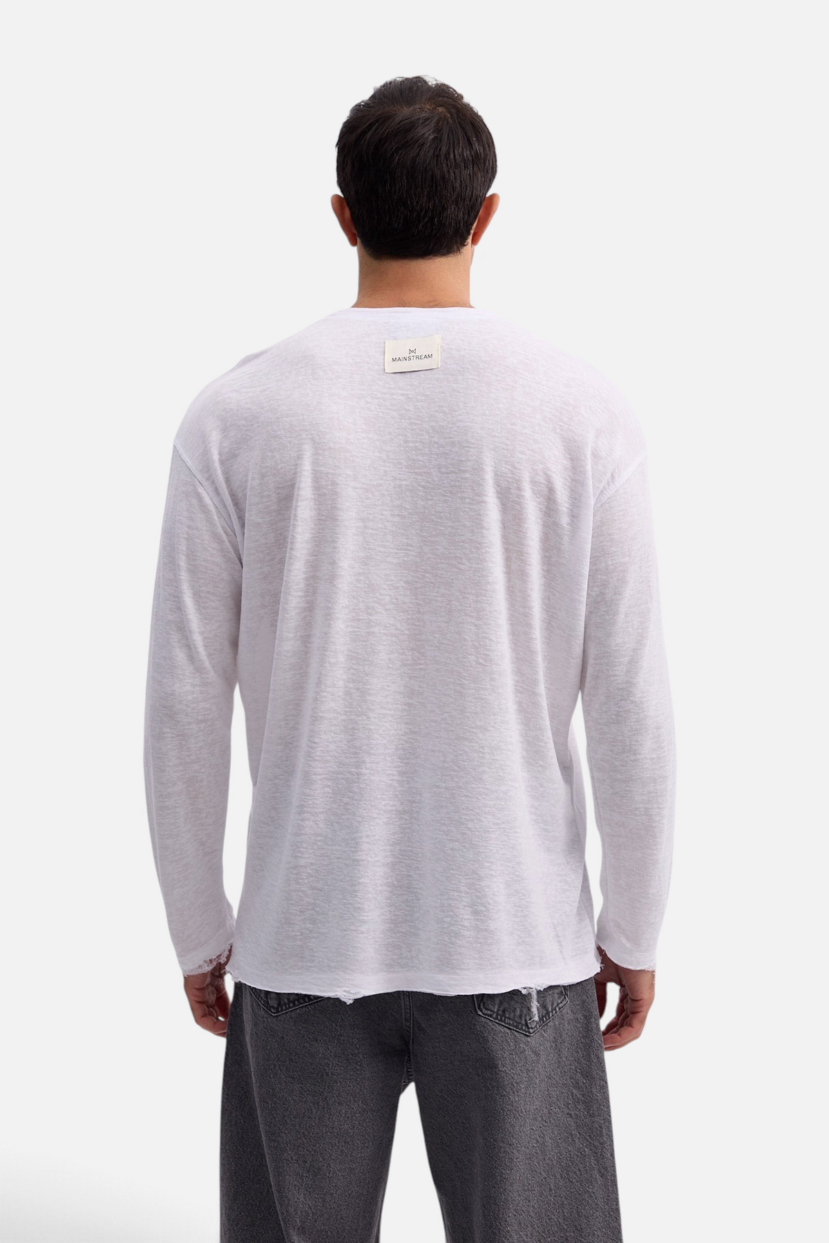Back view of a man wearing a white Mainstreamonline long sleeve linen slub t-shirt with an oversized fit.