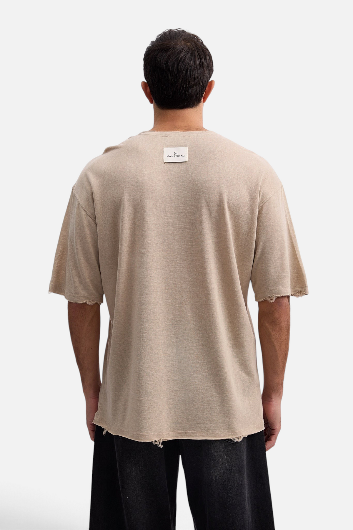 Back view of a man wearing a beige Mainstreamonline oversized linen t-shirt with distressed raw hem details.