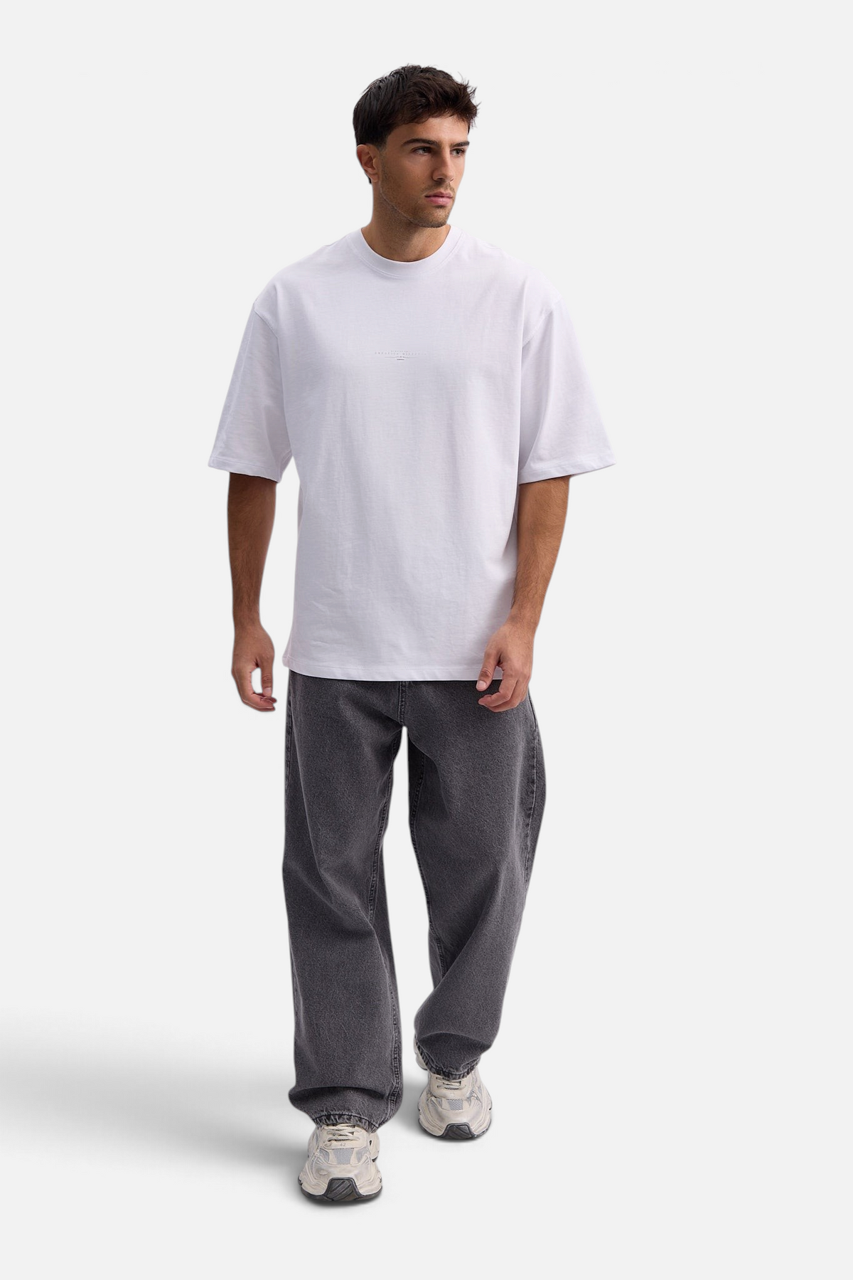 Mainstreamonline white oversized t-shirt worn by a male model with grey jeans and sneakers against a white background