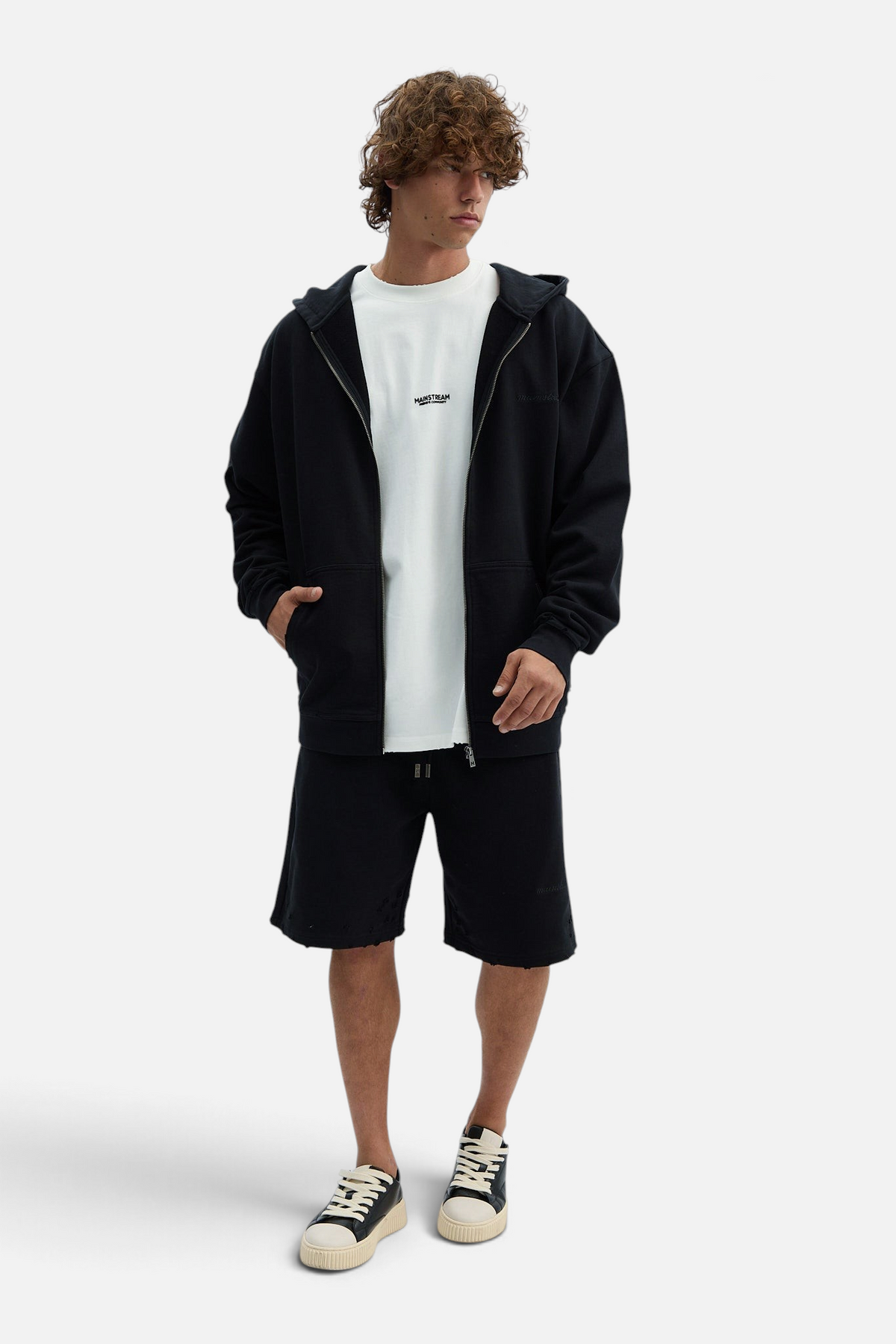 Mainstreamonline Rifts oversized black zip-up hoodie worn by a model with matching black shorts and white sneakers