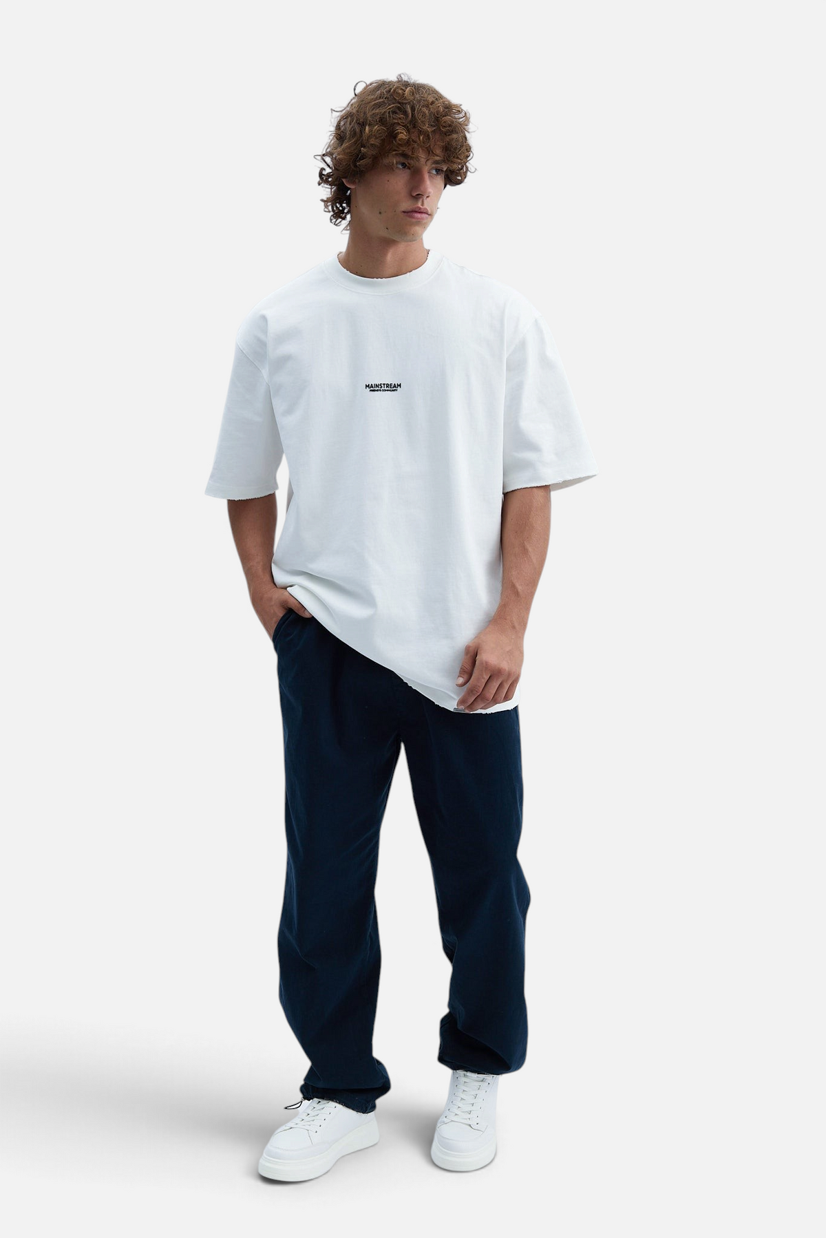 Mainstreamonline baggy jeans in dark blue denim with a loose, relaxed fit worn by a man with curly hair