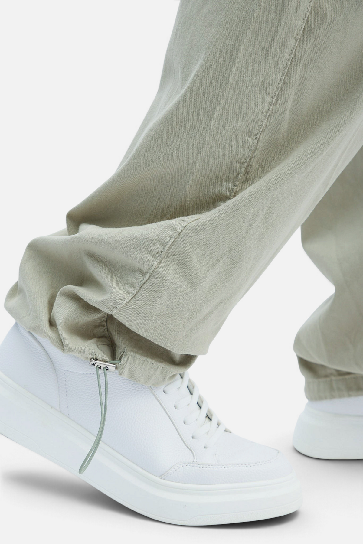 Mainstreamonline baggy jeans in light olive green with adjustable drawstring cuffs worn with white sneakers