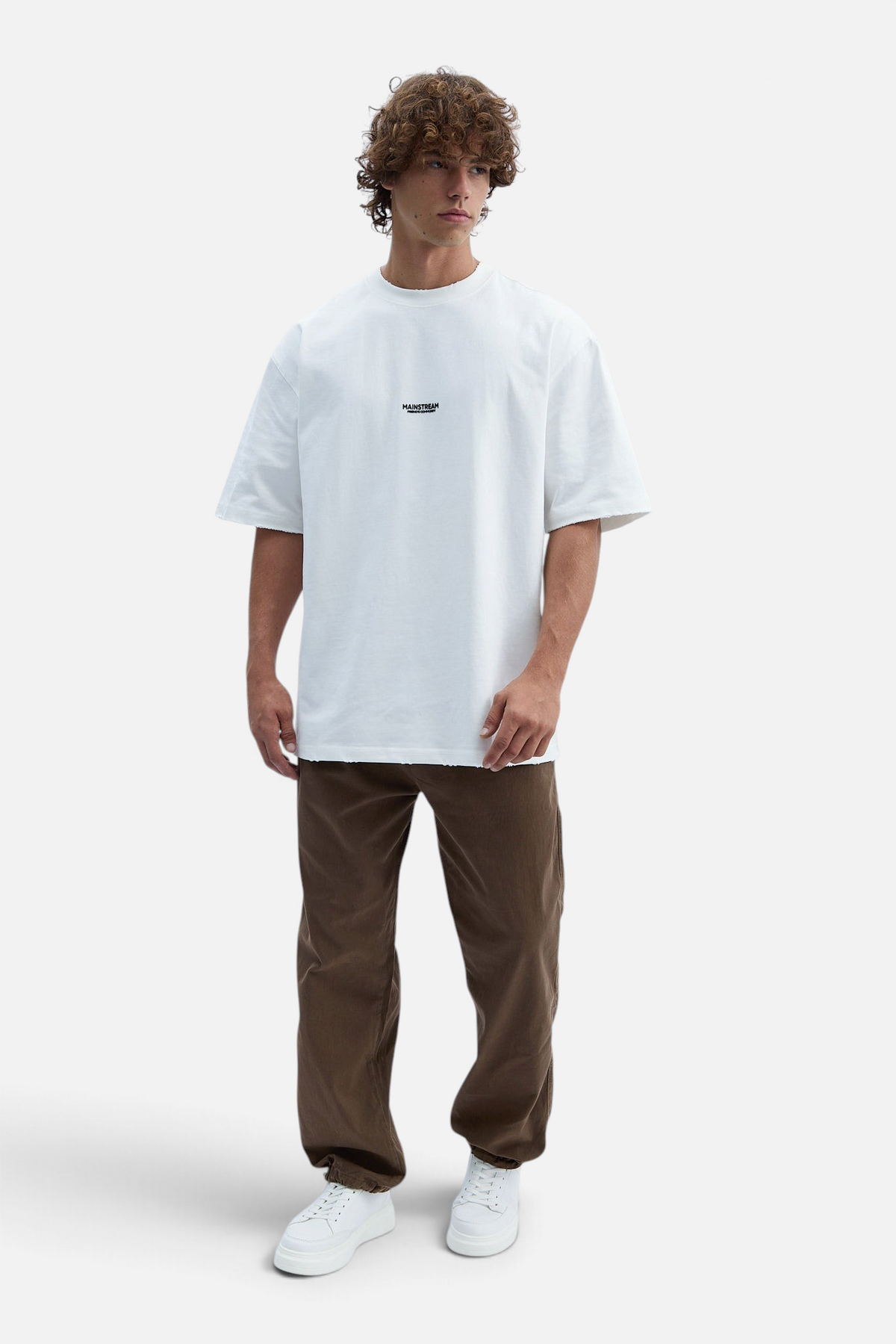 Mainstreamonline model wearing baggy brown jeans and a white oversized t-shirt with a relaxed fit
