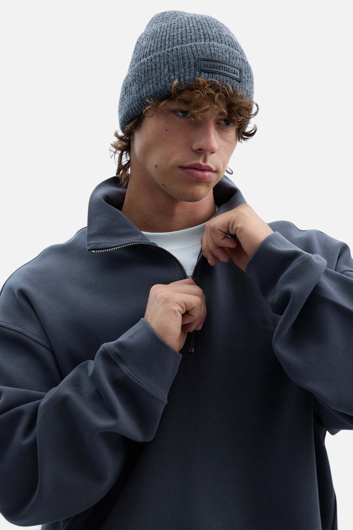Mainstreamonline charcoal grey ribbed knit beanie with a branded rubber patch worn by a young man