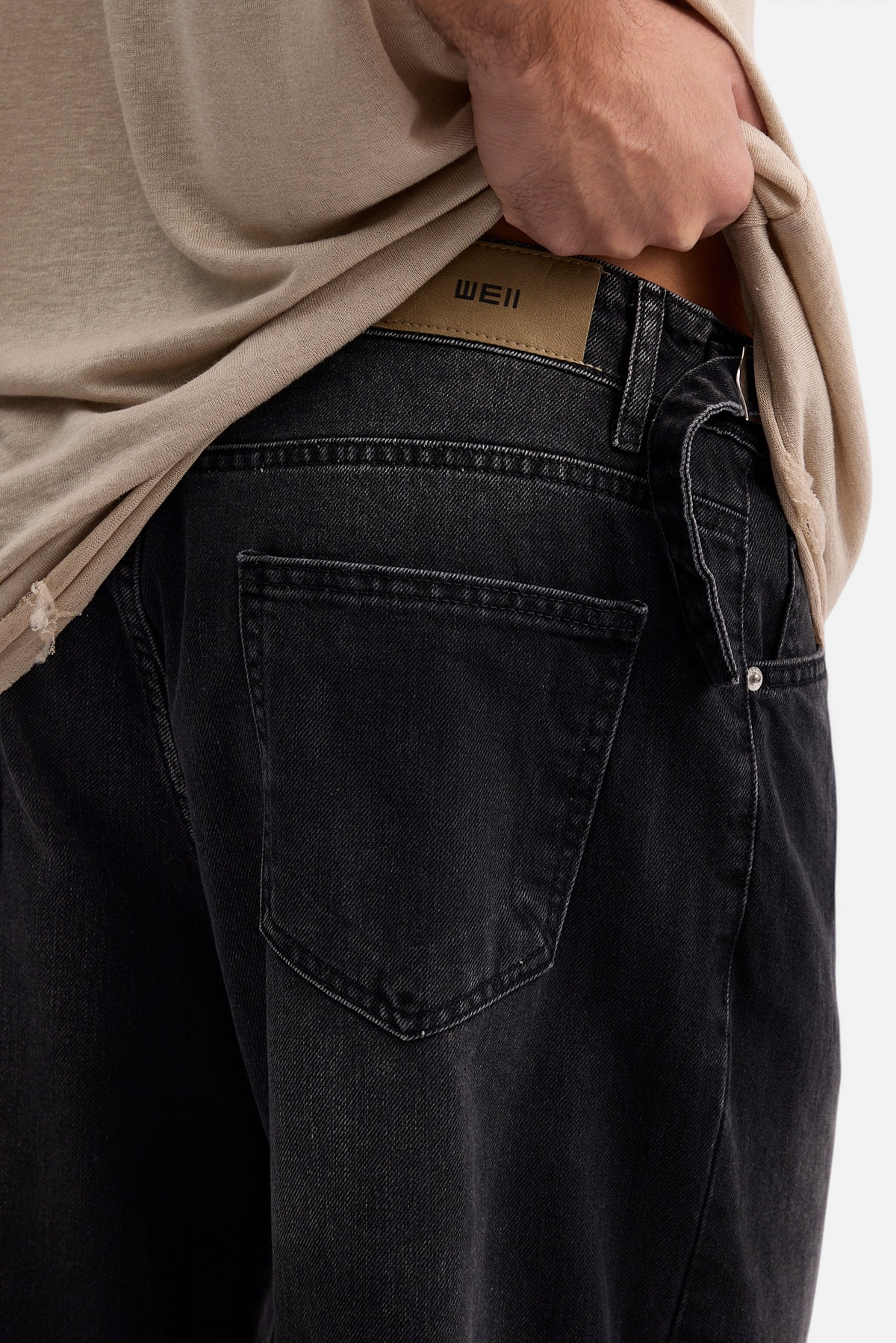 Mainstreamonline black baggy skater jeans with a relaxed fit, featuring a tan leather-look brand patch on the back.