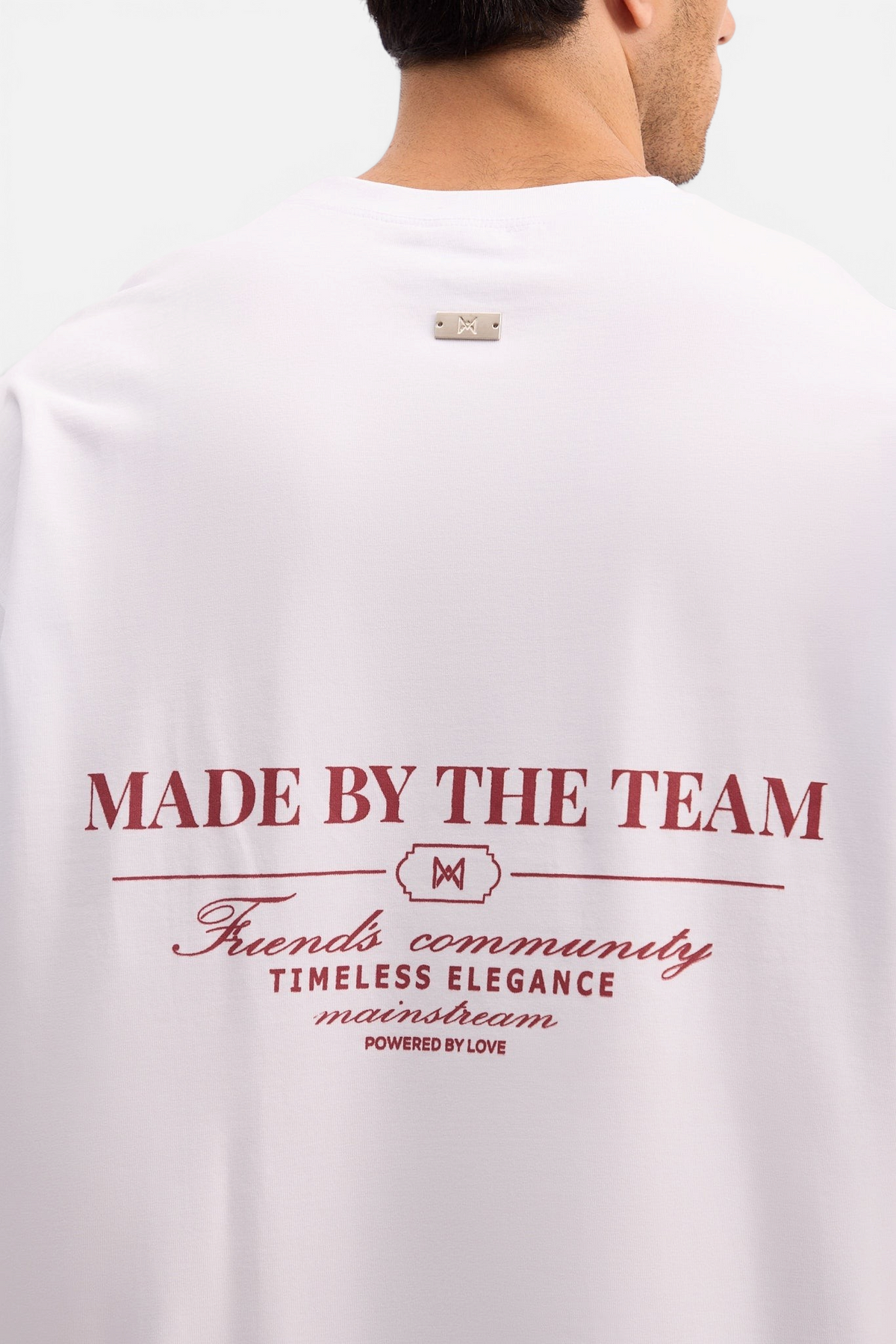 Mainstreamonline white oversized t-shirt with Made By The Team graphic print and metal logo detail on the back