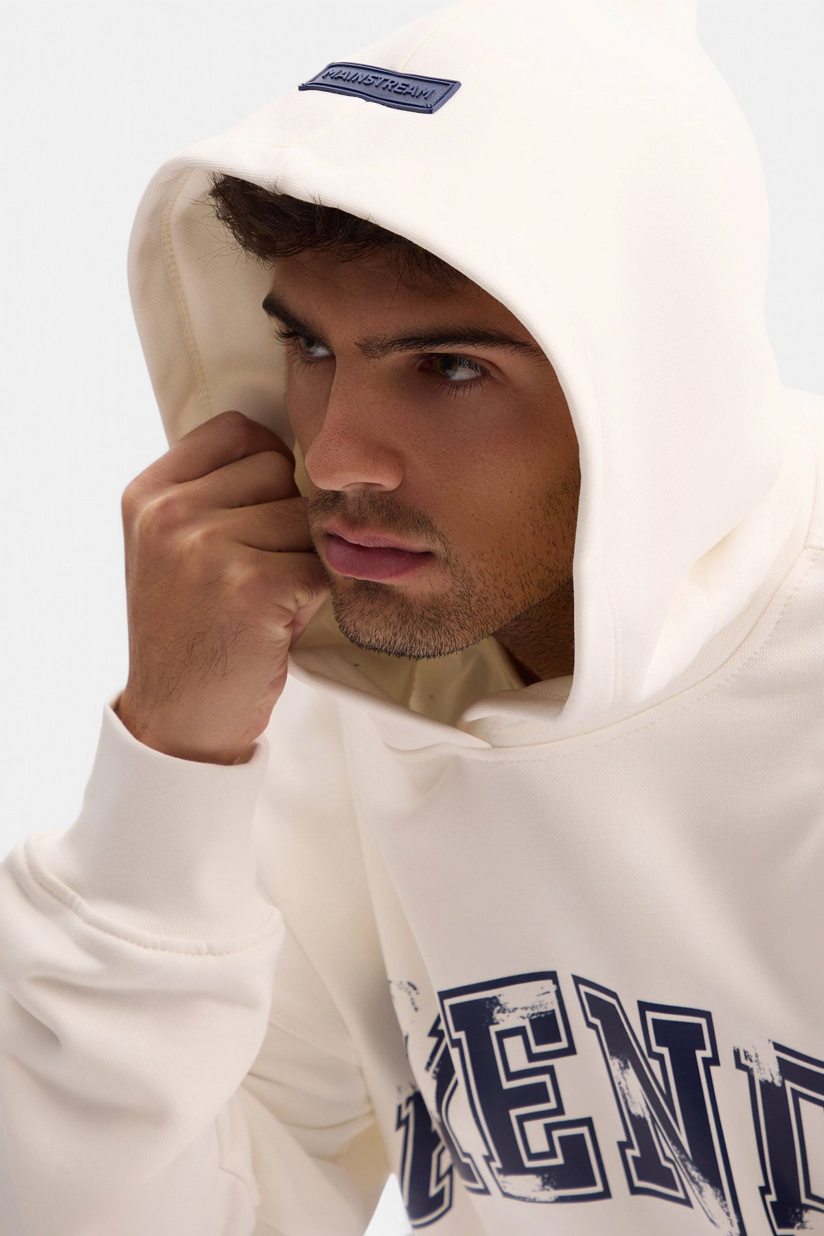 Mainstreamonline oversized cream hoodie with a navy blue logo patch on the hood and distressed graphic print