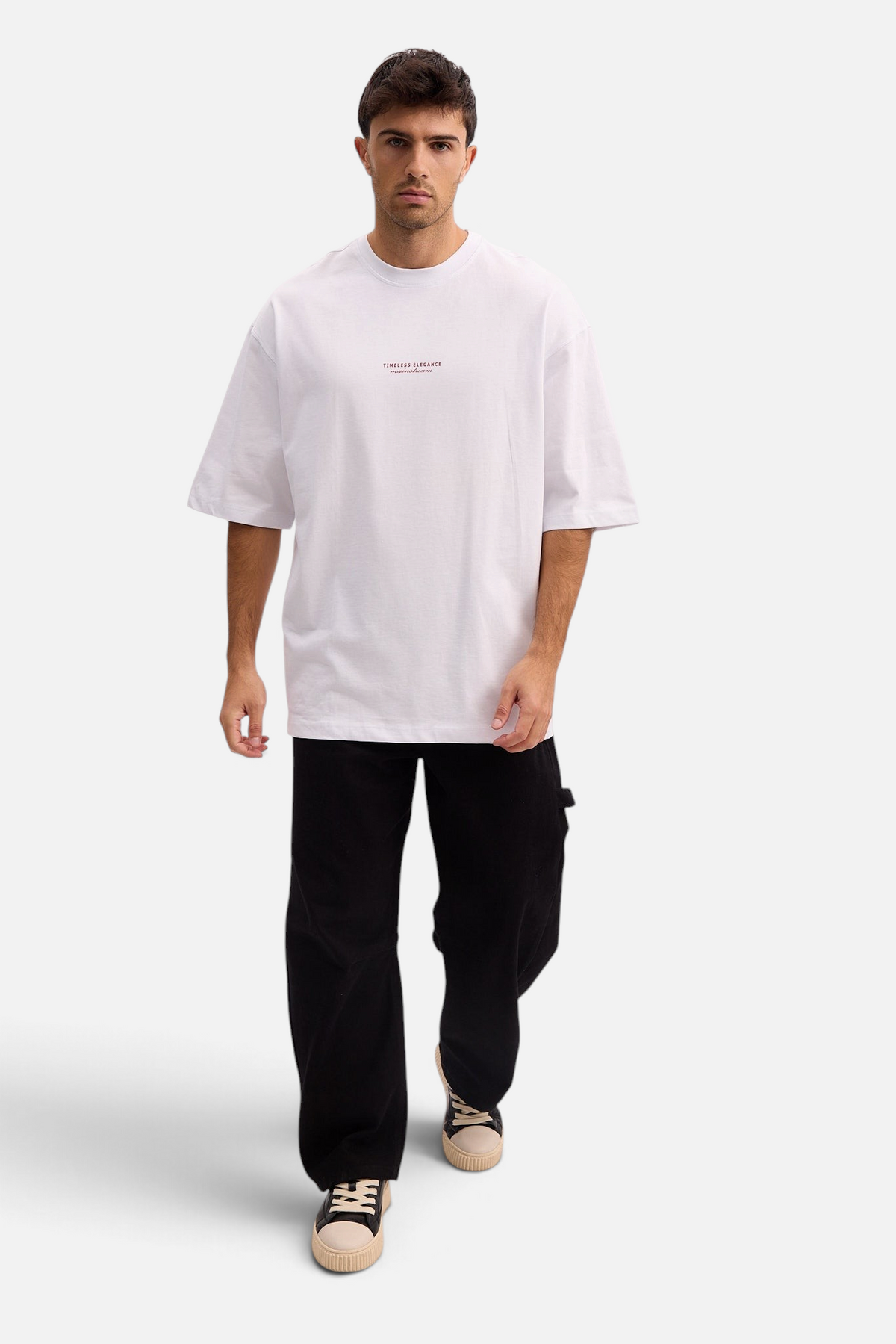 Mainstreamonline white oversized t-shirt with small chest text, worn by a male model with black pants