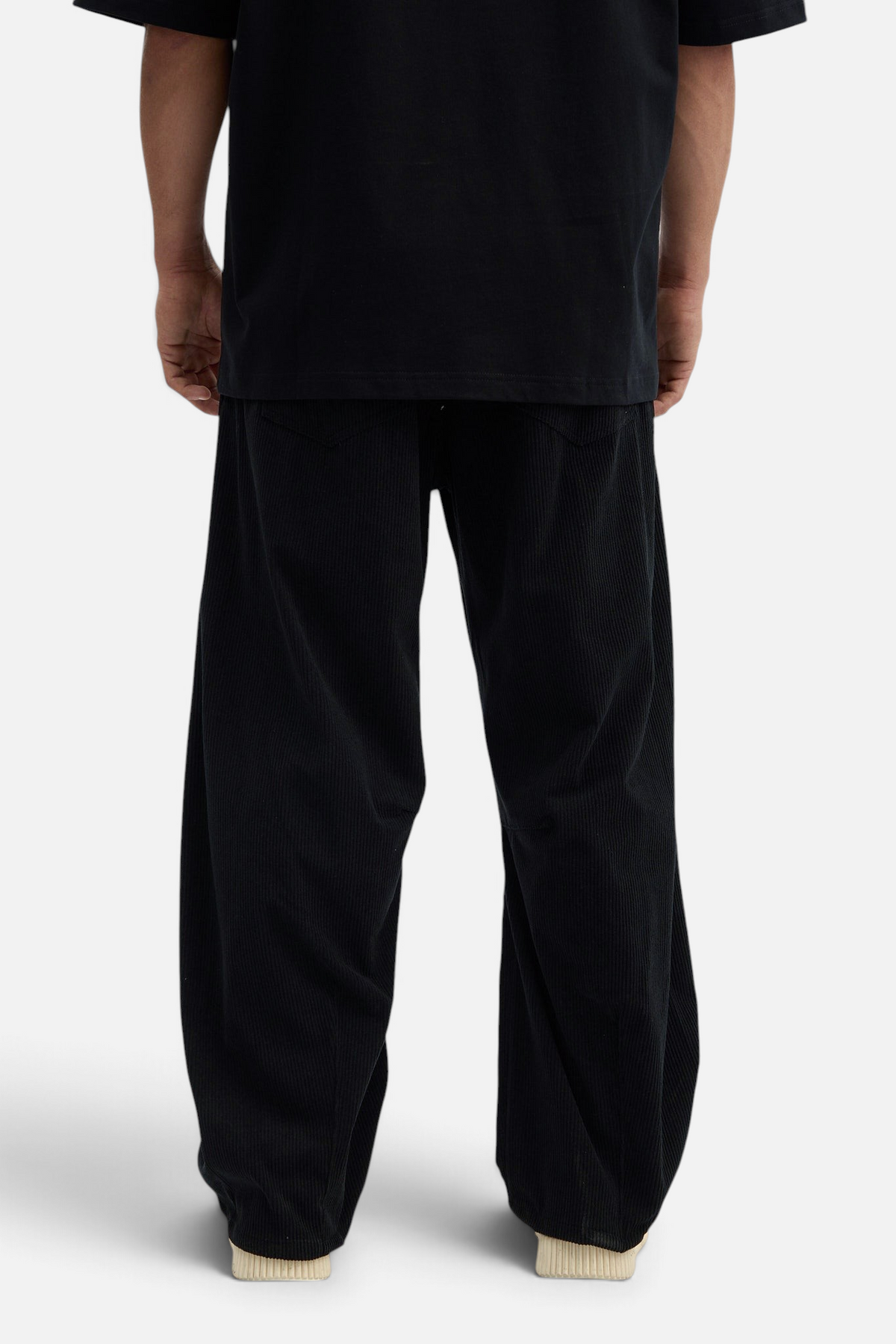 Mainstreamonline black corduroy baggy pants with a loose, relaxed fit worn by a model from the back view.