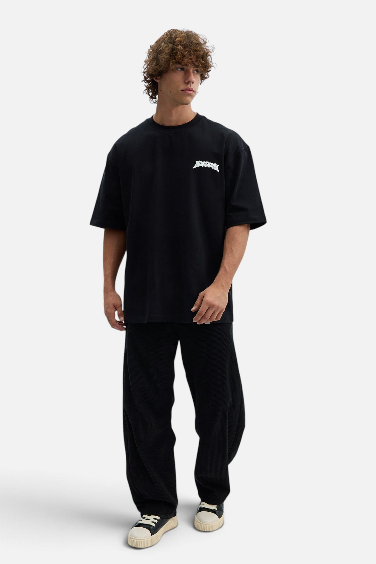 Mainstreamonline black corduroy baggy pants worn by a male model with a black graphic t-shirt and sneakers