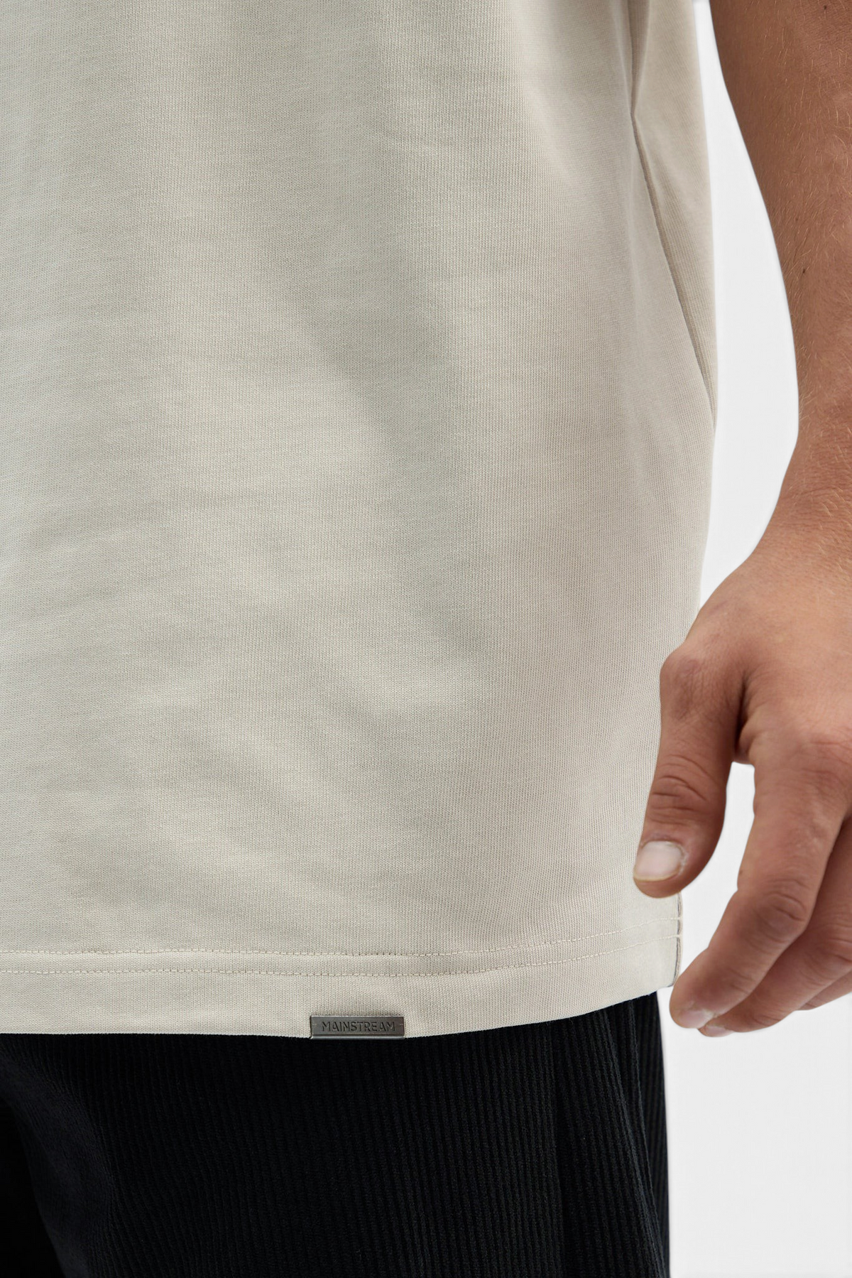 Mainstreamonline beige oversized t-shirt with a clean, relaxed fit and a small branded metal tag at the hem.