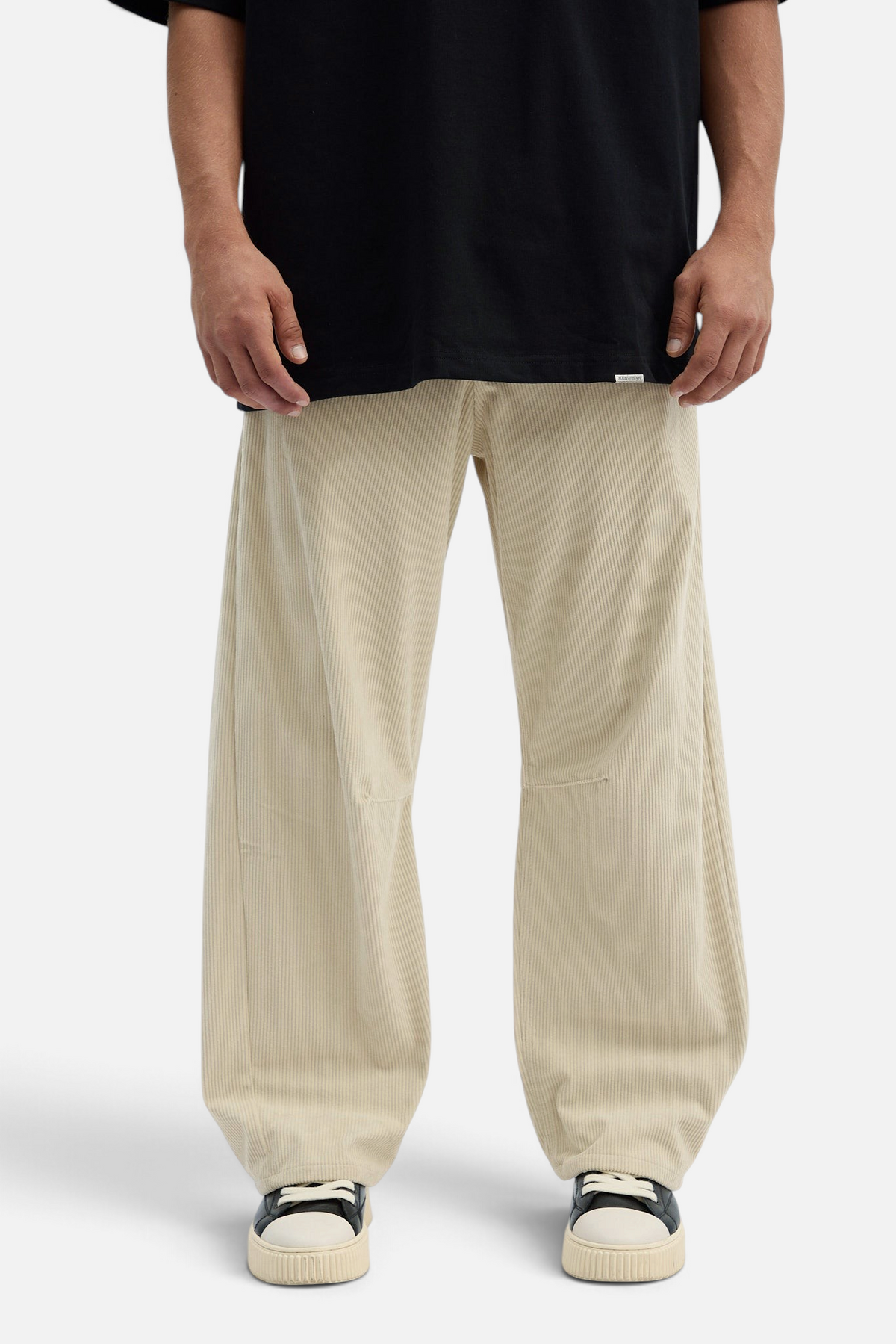 Mainstreamonline beige corduroy baggy pants with a loose, relaxed fit worn with a black t-shirt and sneakers.