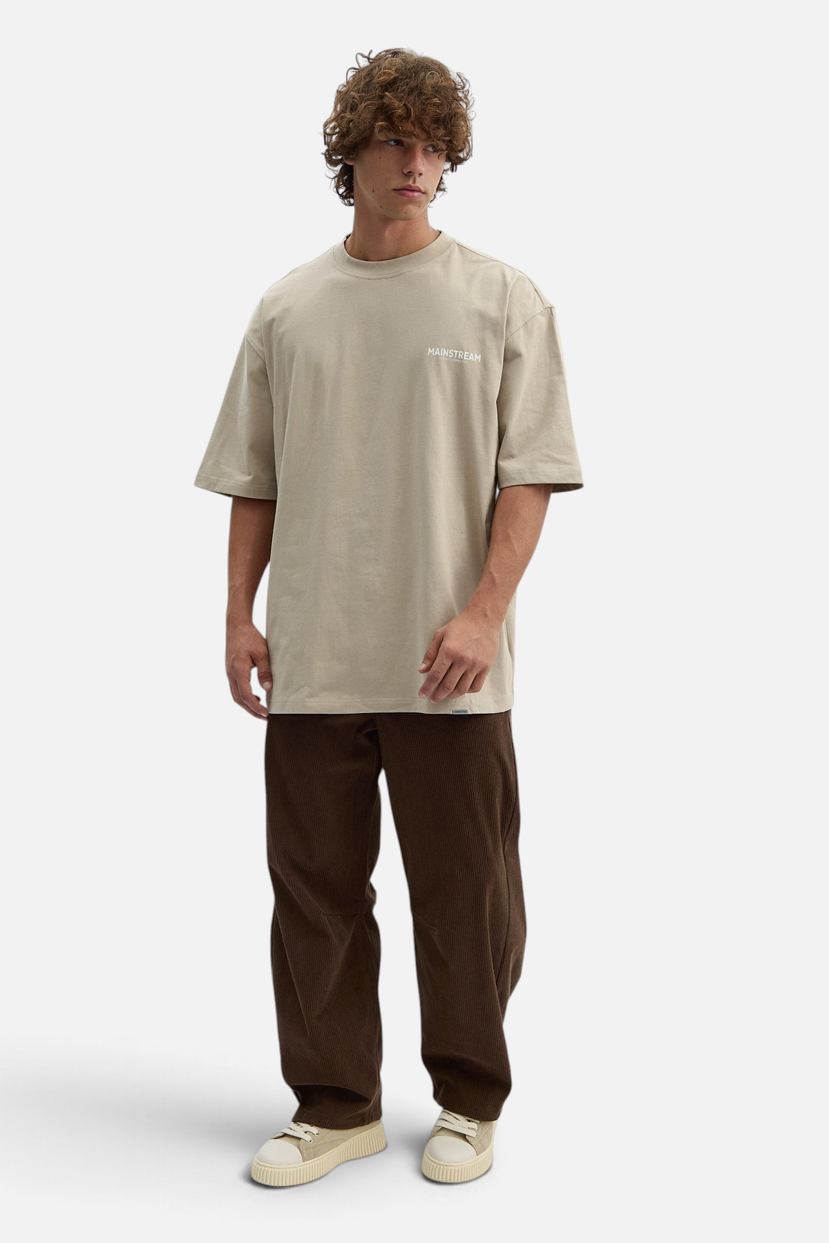 Mainstreamonline model wearing brown corduroy baggy pants and a beige oversized t-shirt with white sneakers