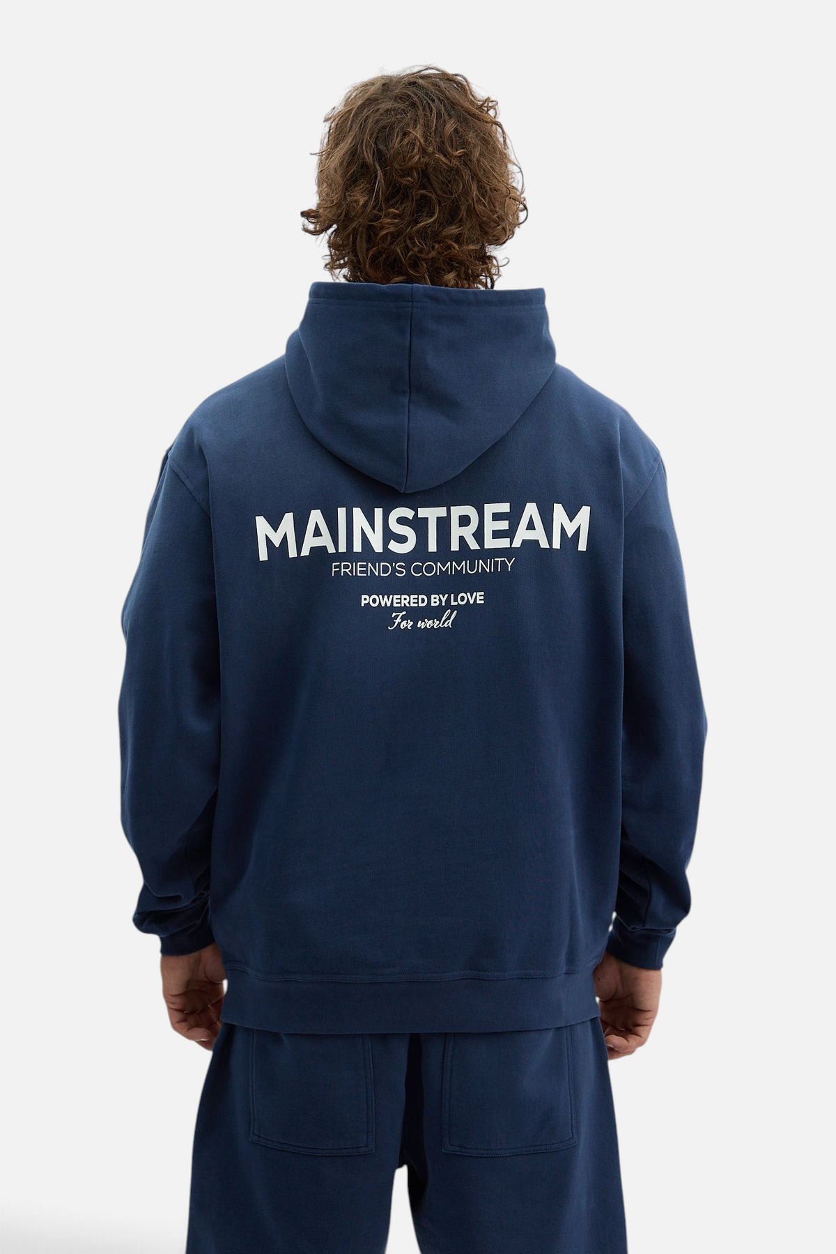 Mainstreamonline oversized navy blue hoodie with white graphic text on the back, worn by a man from behind.
