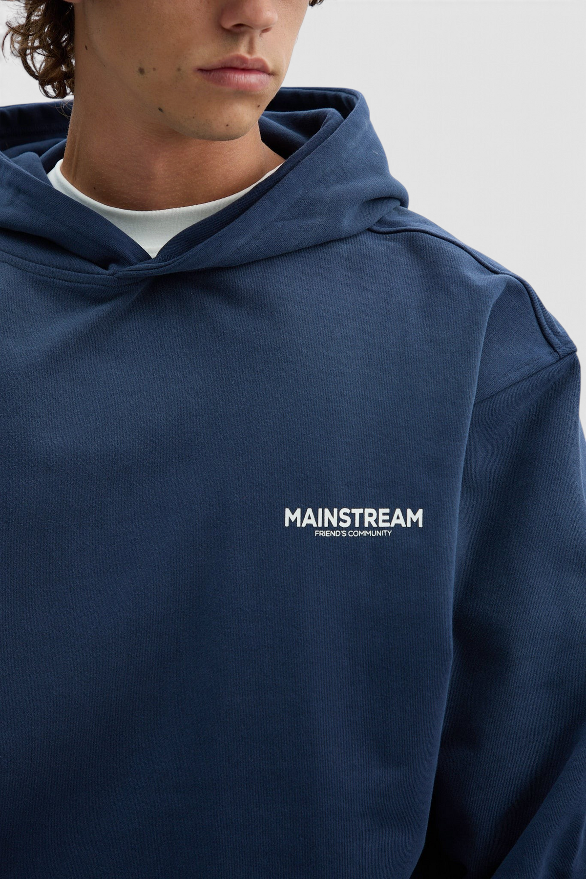 Mainstreamonline oversized navy blue hoodie with white logo print on the chest, worn by a model.