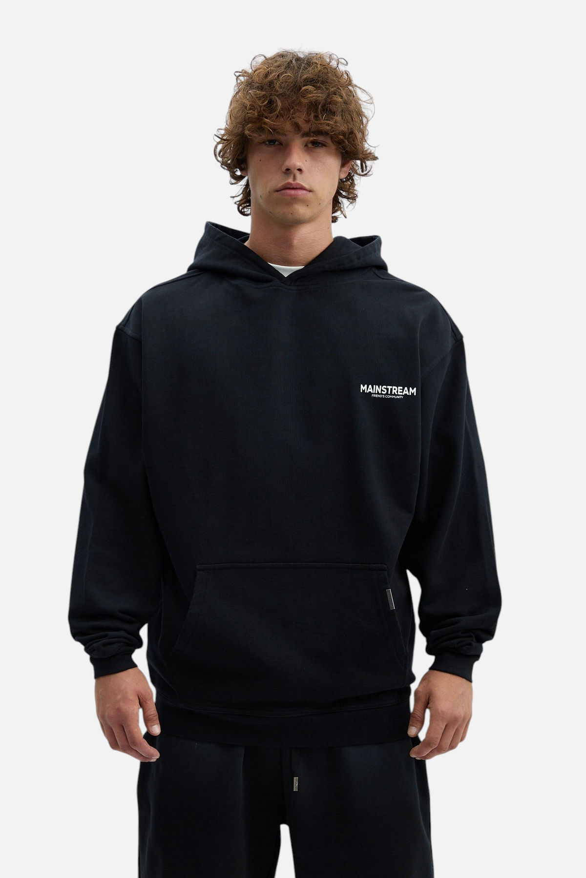 Mainstreamonline oversized black hoodie with a relaxed fit and small white chest logo worn by a male model