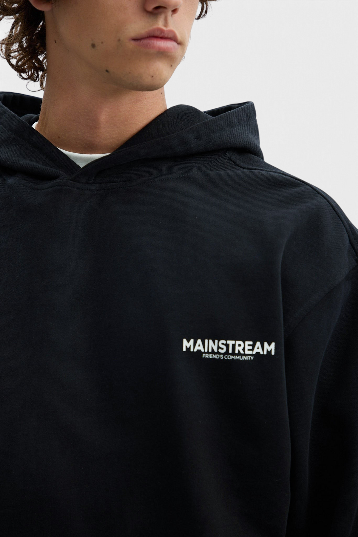 Mainstreamonline oversized black hoodie with white logo print on chest worn by a model