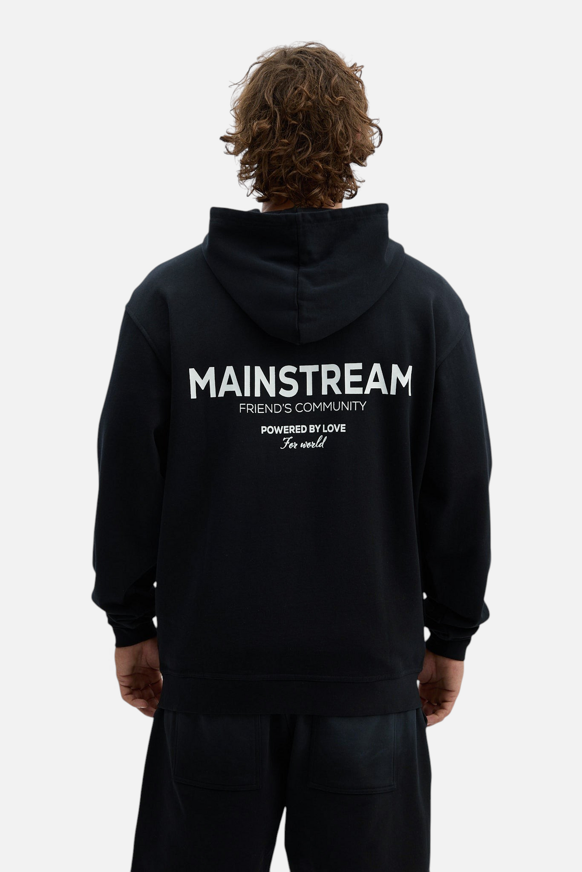 Back view of a man wearing a black Mainstreamonline oversized hoodie with white graphic text on the back
