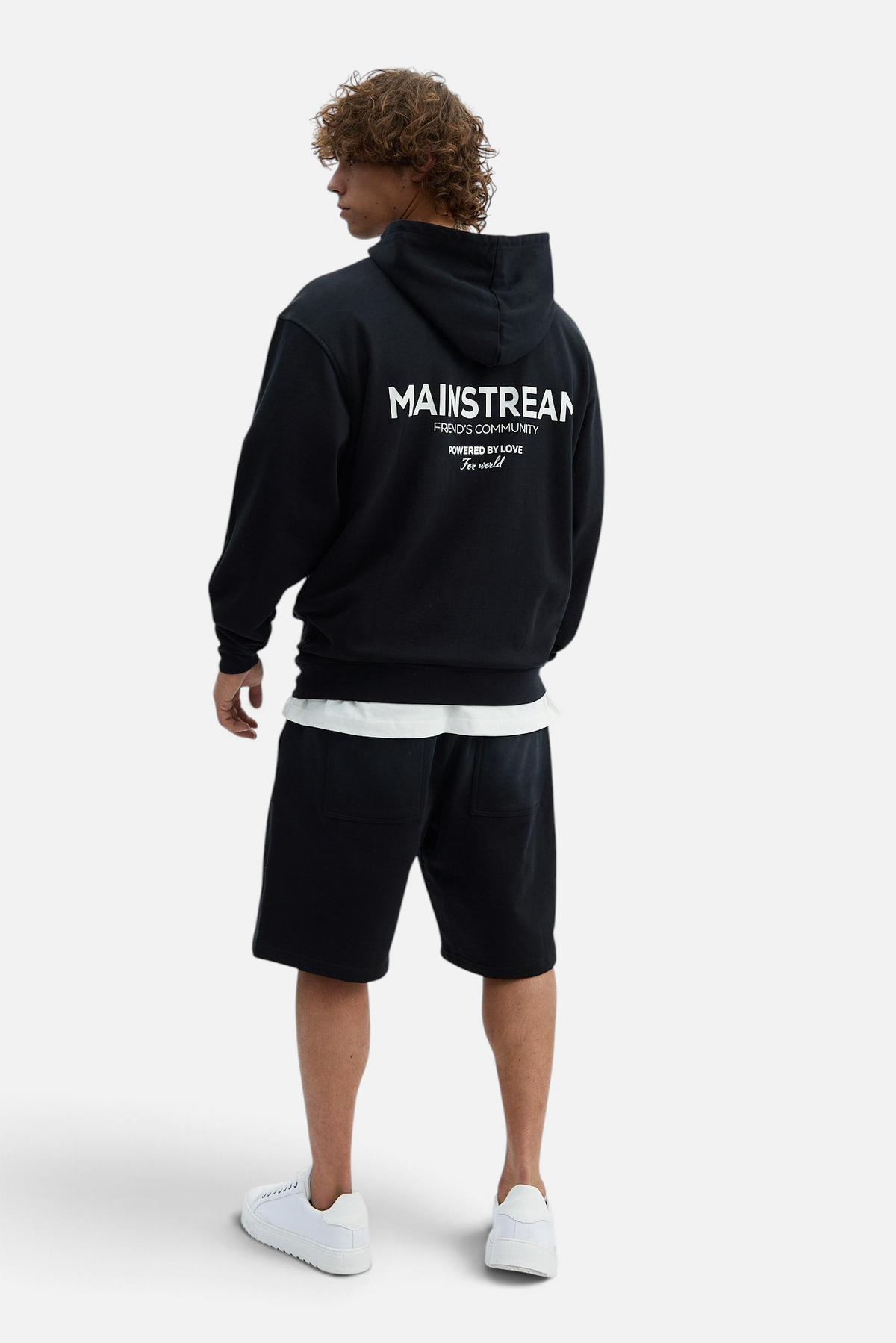 Mainstreamonline oversized black hoodie with white back graphic print worn by a man with shorts and white sneakers