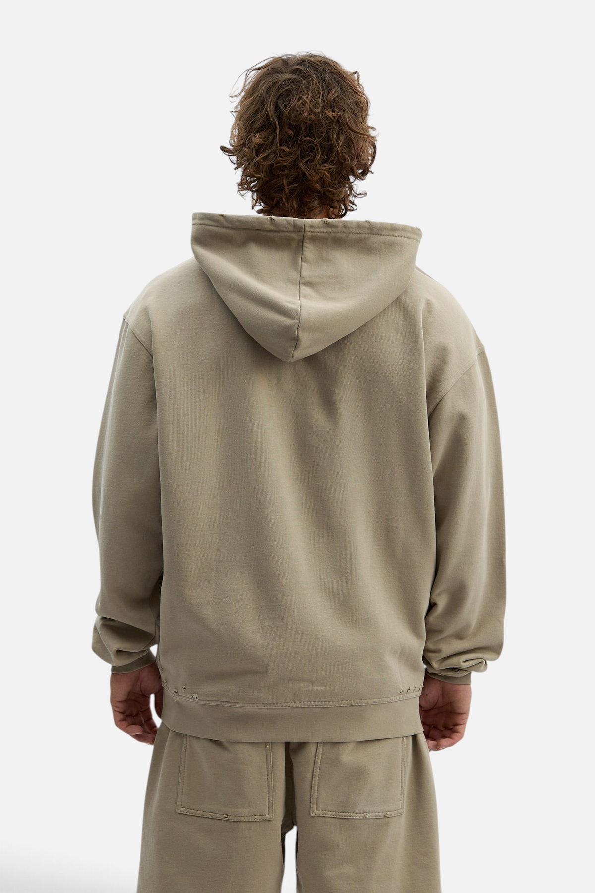 Back view of a man wearing a Mainstreamonline Rifts oversized beige hoodie with a relaxed fit and distressed hem