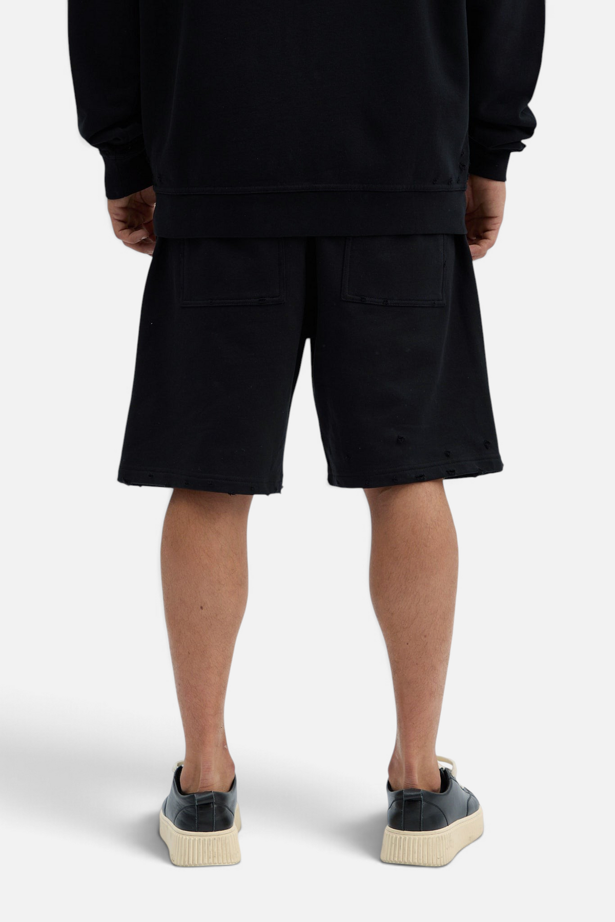 Mainstreamonline black distressed cotton shorts with raw hem and back pockets worn by a model