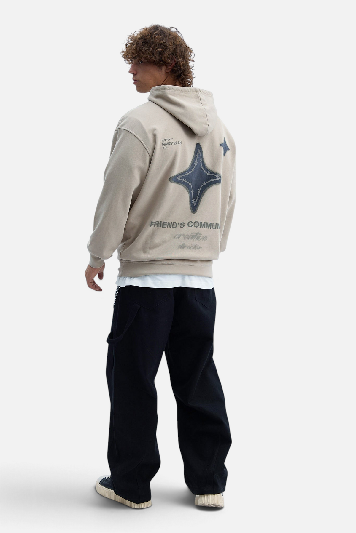 Mainstreamonline oversized beige hoodie with a star graphic on the back worn by a man with curly hair