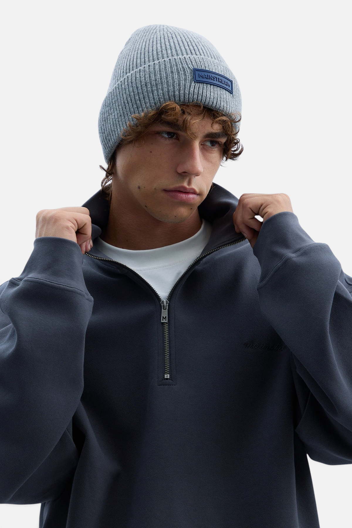 Mainstreamonline grey ribbed knit beanie worn by a young man in a dark grey quarter-zip sweatshirt