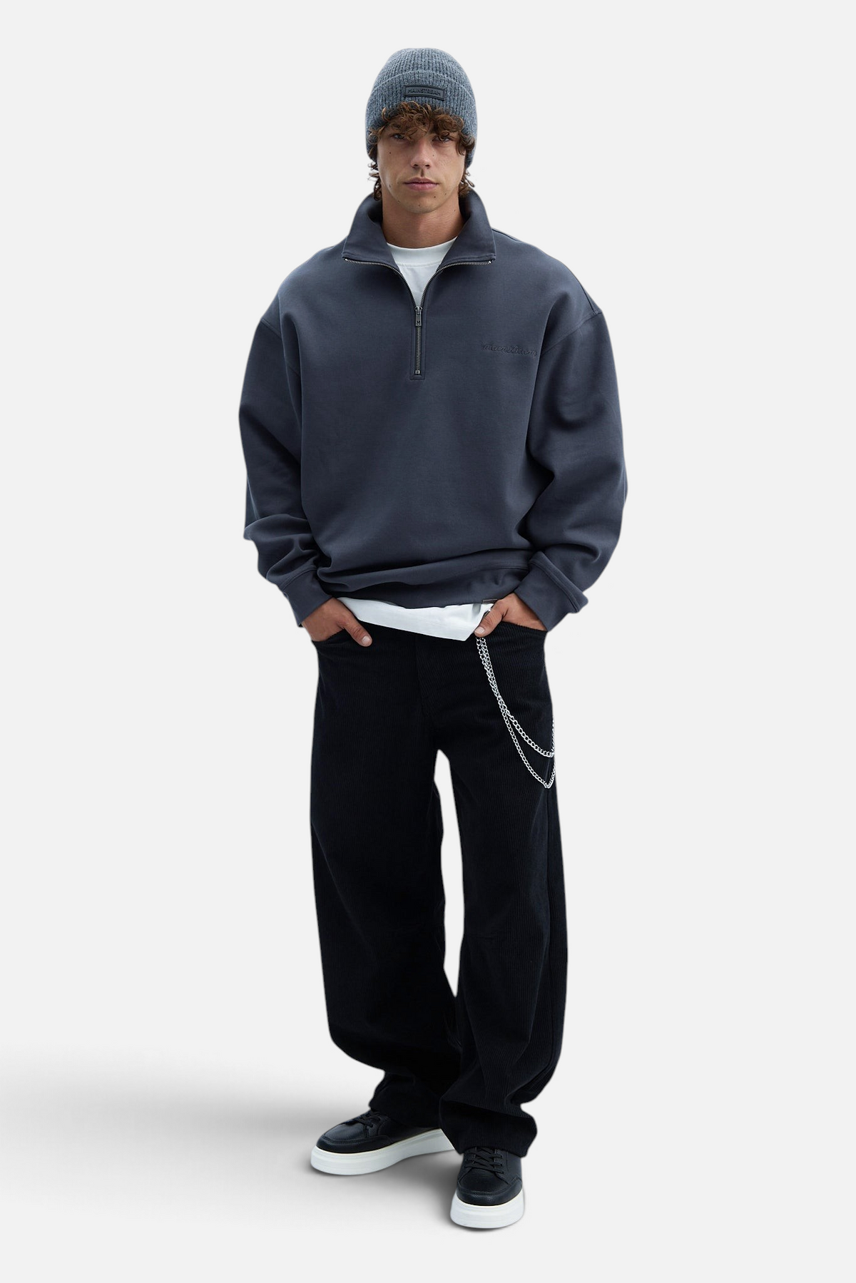 Mainstreamonline model wearing a grey wool beanie, charcoal quarter-zip sweatshirt, and black pants with a chain.