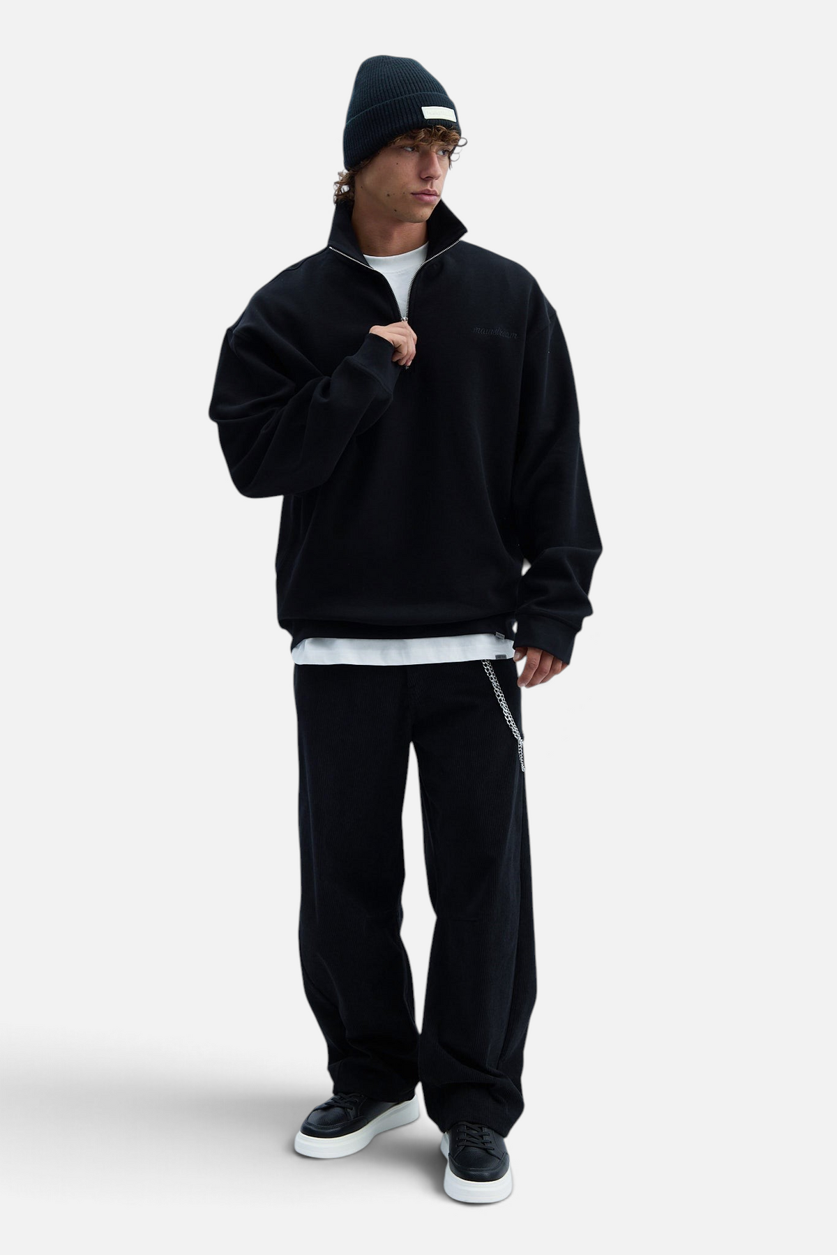 Mainstreamonline black wool beanie worn by a male model in a casual streetwear outfit with a quarter-zip sweatshirt